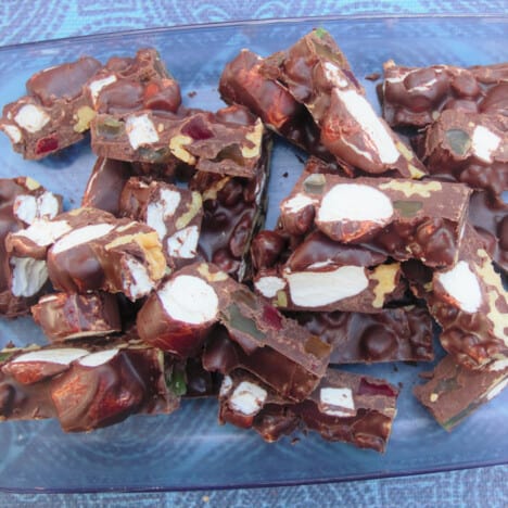 Chunks of the cooled chocolate rocky road lay on a blue glass serving plate on a blue tablecloth.