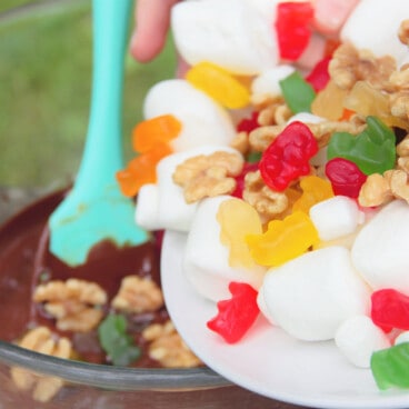 Marshmallows, candy, and walnuts are being poured into a bowl containing the chocolate and peanut butter mixture.