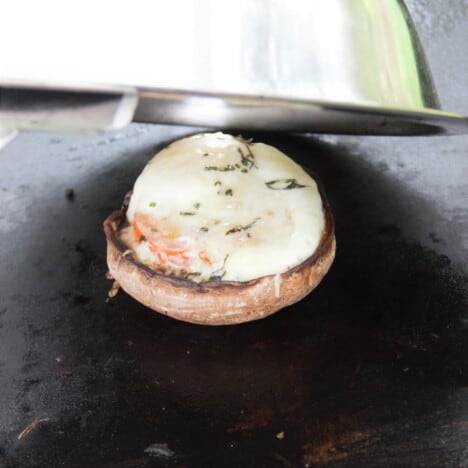 A stainless heating done being lifted off the egg in a mushroom to reveal it cooked and the cheese melted.