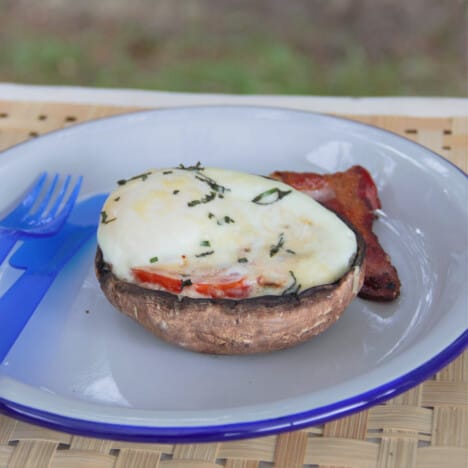 A camp plate with the egg filled mushroom and a side of bacon.