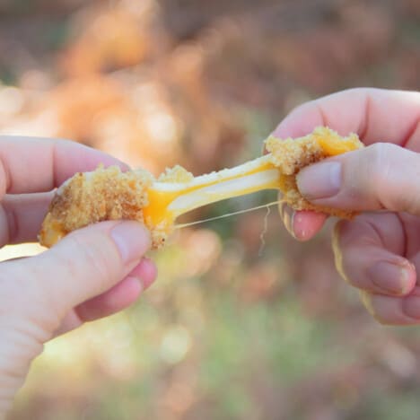 A Mozzarella Stick being pulled in half exposing the gooey cheese inside which is stringing between the two halves.