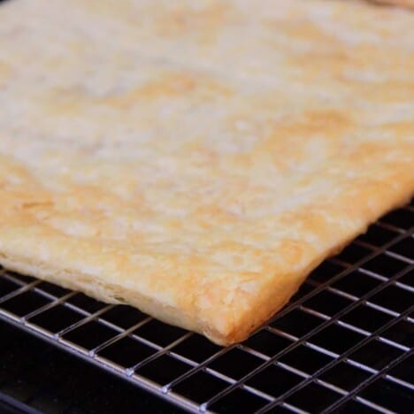 A golden brown sheet of cooked puff pastry sitting on a cooling rack.