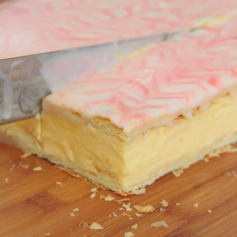 A slab of vanilla slice being cut into serving pieces with a large slicing knife.