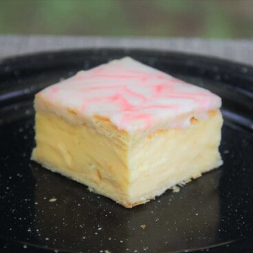 A single square serving of vanilla slice sitting on a black camp plate.