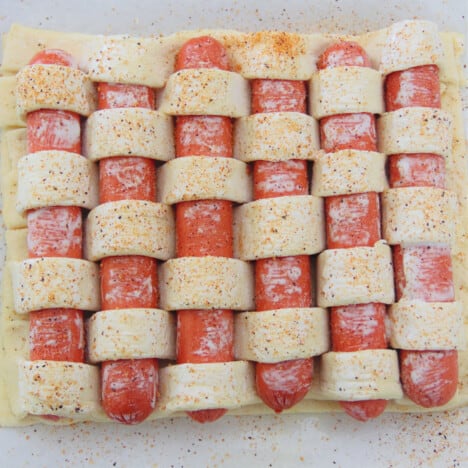Looking down on an unbaked hot dog tart, sprinkled with rub, to show the weaving pattern.
