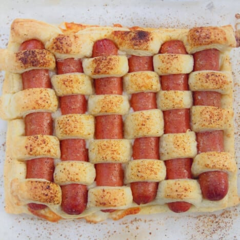 Looking down onto a golden brown baked hot dog tart on white parchment paper.