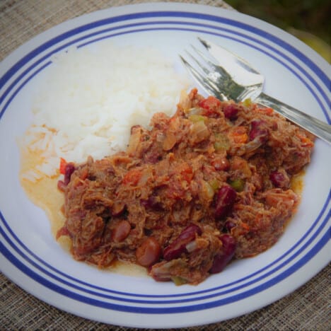 Looking down on a large helping of leftover brisket chili is served alongside a scoop of white rice on a white plate with blue trim.