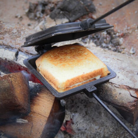 A pie iron being cracked open next to the camp fire showing a golden brown pie iron hot dog.