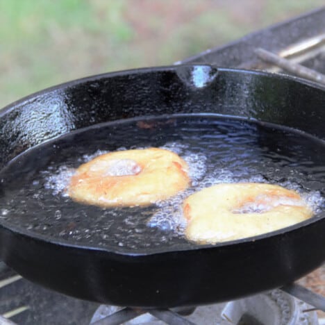 A skillet with two pineapple fritters being shallow fried.
