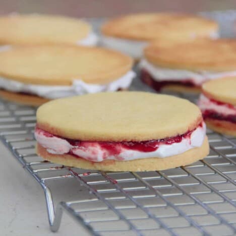 Looking onto a cooling rack with wagon wheel cookies, with the marshmallow and jam layers, but not yet dipped in chocolate.