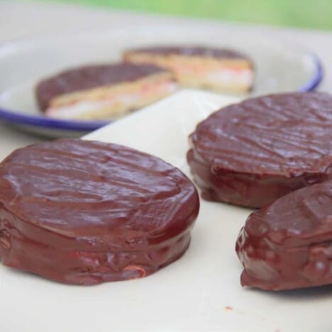 Looking across a white table with three finished wagon wheel cookies, with a plate with a halved cookie in the background.