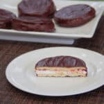 A halved wagon wheel sits on a white plate in the foreground, while four whole wagon wheel cookies sit on a white plate in the background.