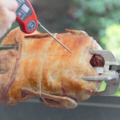 A golden brown rotisserie duck with a digital thermometer in it checking the temperature.