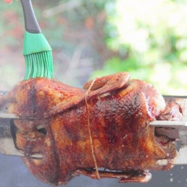 The duck on a rotisserie with the 5-spice glaze being added with a green brush