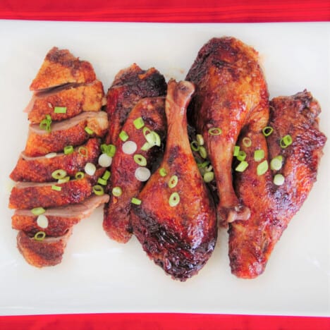 Looking down on a portioned duck with a mahogany colored glaze and sprinkled with fresh sliced spring onions.