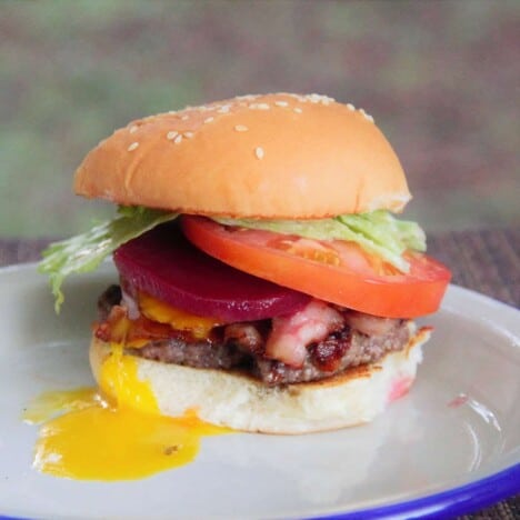 A fully cooked Aussie smash burger is on a camp plate with a yellow egg yolk oozing out.