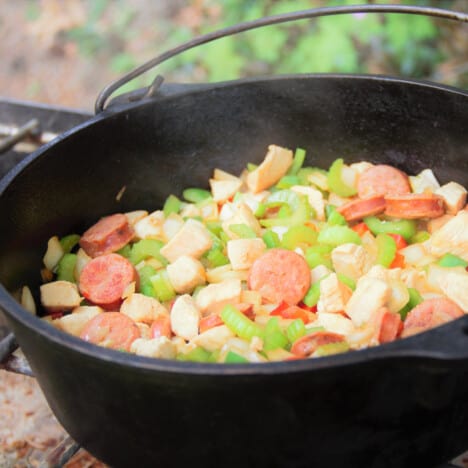 A Dutch oven is filled with the bright colors of the fresh bell peppers, celery, and sausage before it is cooked.