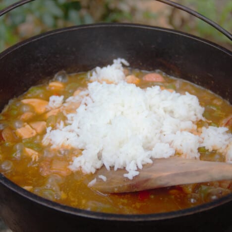 A Dutch oven is filled with the jambalaya base with the cooked white rice being stirred throughout.