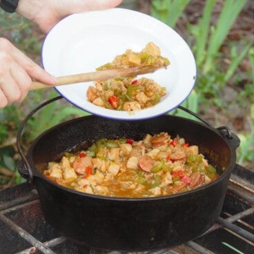 A serving of Camping Mock Jambalaya being served into a camp bowl from a Dutch oven.