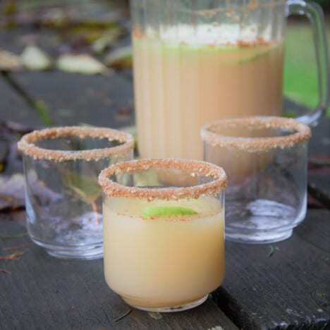 A picnic table with a caramel apple mocktail, pitcher of same mocktail, and two rimmed but empty glasses.