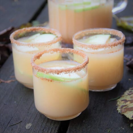 Three glasses of caramel apple mocktail ready to serve with a half full pitcher in the background.