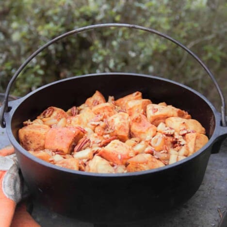 A Dutch oven sits on a picnic bench filled with baked caramel apple monkey bread.