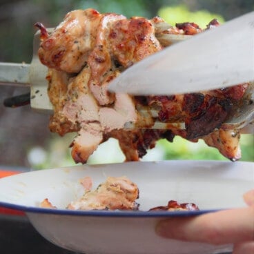 A rotisserie of gyro chicken with a serving being sliced off onto an enamel camp plate.