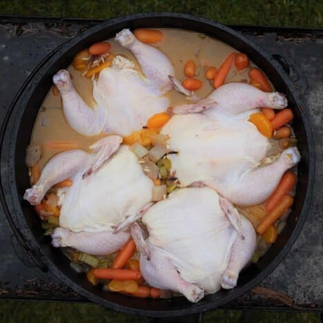 Four raw Cornish game hens are in a Dutch oven, surrounded by broth and carrots.
