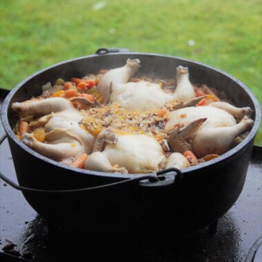 A large Dutch oven filled withe the orange wild rice with four Cornish game hens within it.