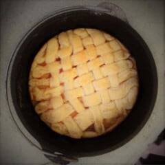 Looking down into a Dutch oven with a lattice pie crust topping with peeks of apple pie filling.
