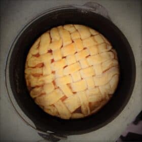 Looking down into a Dutch oven with a lattice pie crust topping with peeks of apple pie filling.