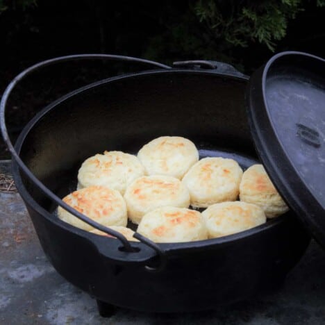 A Dutch oven with its lid off leaning on the main part is filled with golden brown cooked biscuits.