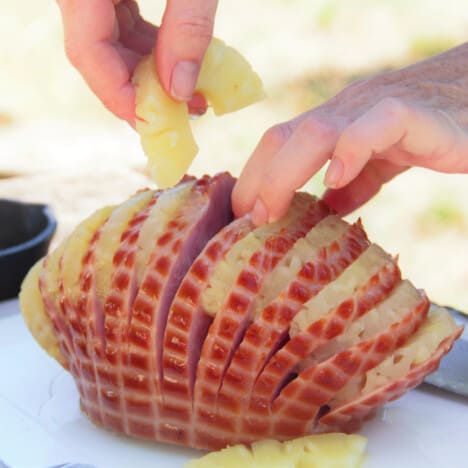 A chopping board with the last slice of pineapple being inserted into the ham.