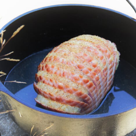 A sliced ham with pineapple rings sits in a Dutch oven surrounded by pineapple juice.