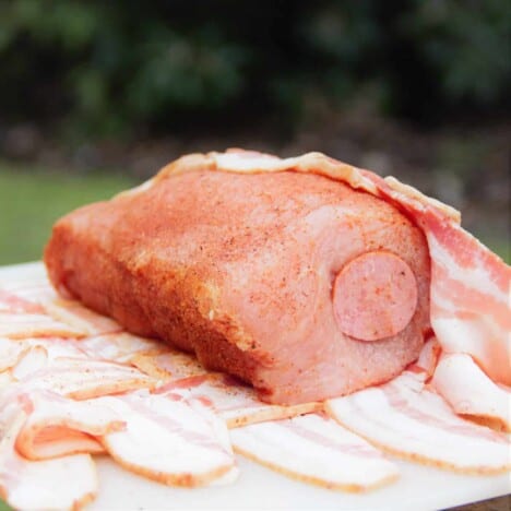 A raw pork loin stuffed with the Kielbasa sausage and covered in rub being wrapped in the bacon weave.