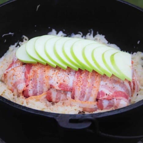Layers of sliced green apple sit atop a bacon-wrapped pork loin in a Dutch oven.
