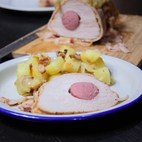A slice of the pork tenderloin with the kielbasa sausage in the center sits on a white camping plate.