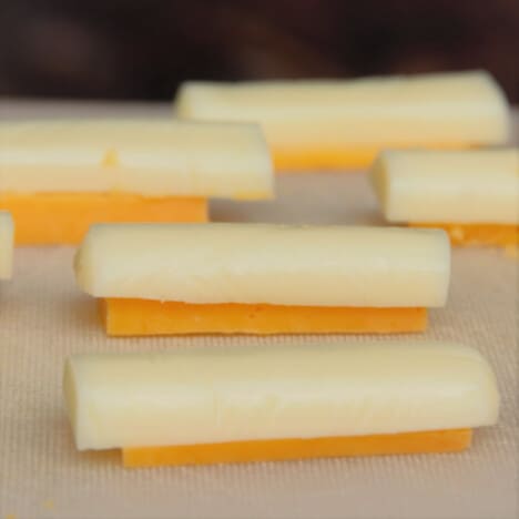 A white chopping board topped with sliced cheese sticks, with cheddar at the base and mozzarella on the top.