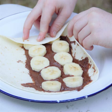 A tortilla wrap with Nutella and banana inside, being folded and ready to grill.