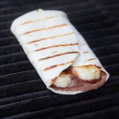 A Nutella banana wrap sittling on the grill showing the filling contents and even golden brown grill lines on the tortilla.