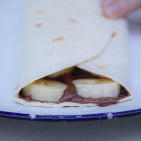 Looking into an ungrilled tortilla stuffed with Nutella spread and sliced bananas.