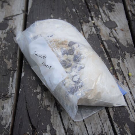 A resealable plastic bag with the dry ingredients for the chocolate chip cookie in it sitting on a picnic table.