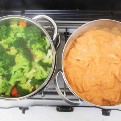 Looking down on a pot wth steamed broccoli and a pot of chicken in peanut sauce on a camp stove.