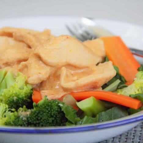 Looking across a camp plate serving of peanut chicken on top of steamed vegetables.