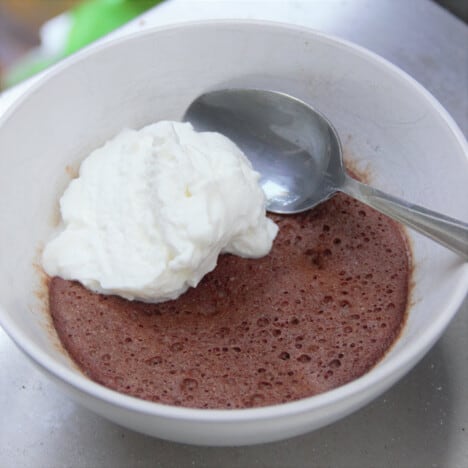 A serving of chocolate protein pudding with a scoop of yogurt in a white bowl with a dessert spoon ready to eat.