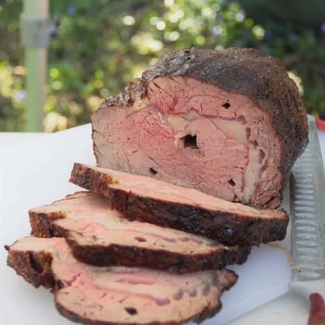 A cooked rib eye roast on a white chopping board with three slices cut off exposing the pink center and spit holes.