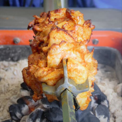 Looking down a spit with tandoori chicken on it over coals.