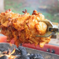 Tandoori chicken on a spit cooking over coals with a small flame flareup.