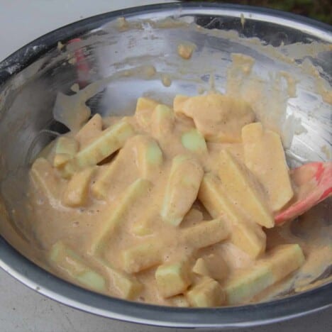 A stainless steel camp bowl is filled with pieces of apple covered in a thick batter.