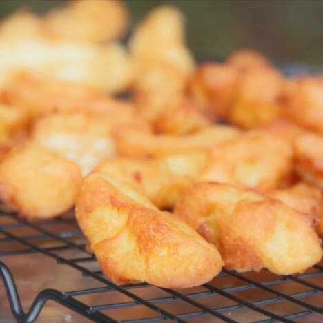 A cooling rack is topped with golden brown apple fritters shaped like chips.